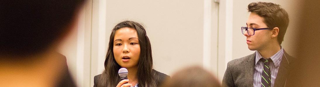 female student holds microphone and male student sits next to her listening