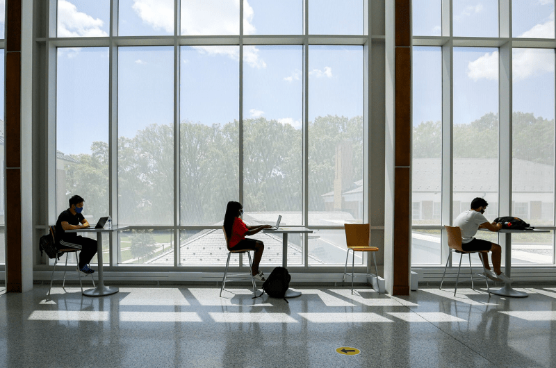 three students at desks in front of large window
