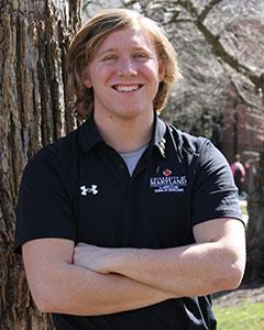 Photo of Owen Mank in black polo shirt standing in front of a tree