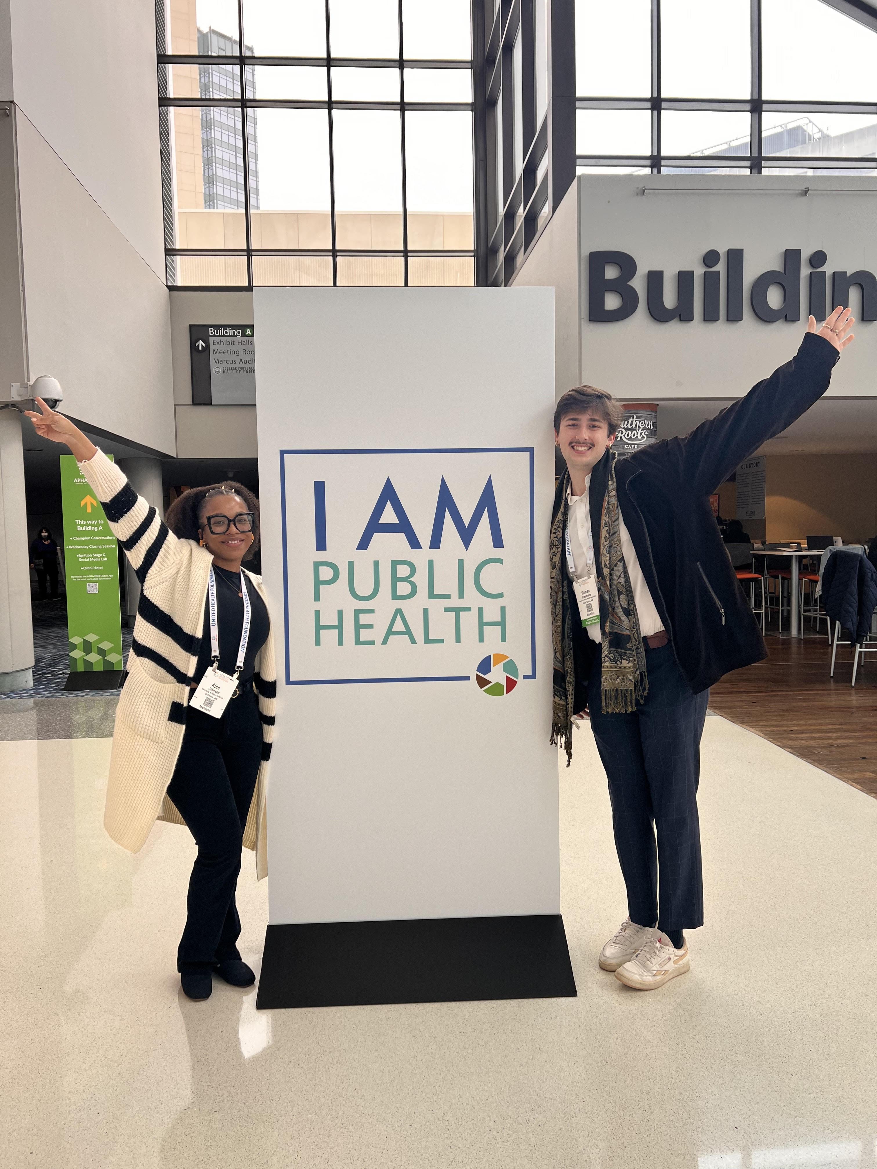 Roman Kassaraba and conference attendee standing on each side of a sign that says "I am Public Health"