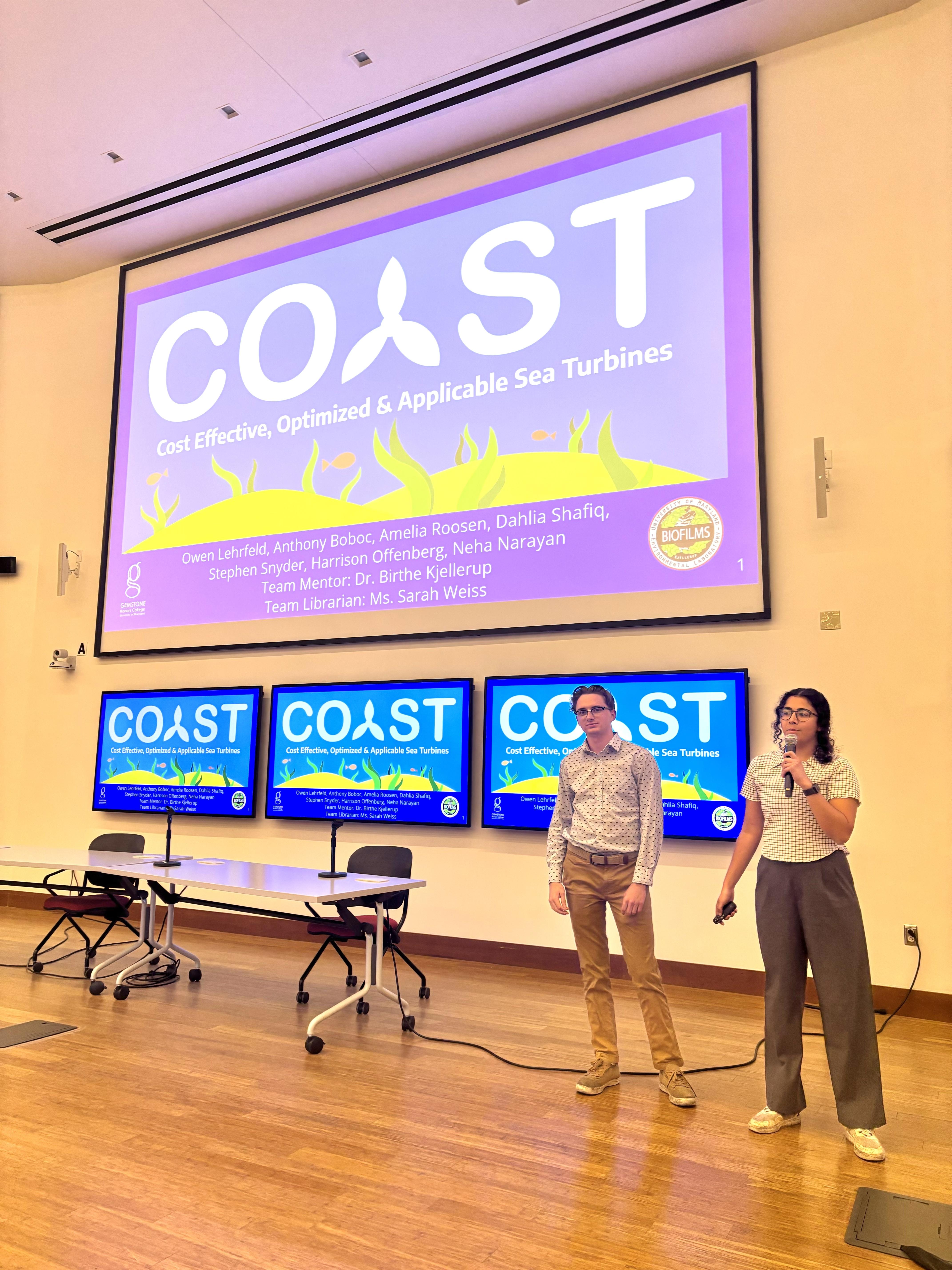 Two students of Team COAST standing in front of a presentation in a lecture hall.