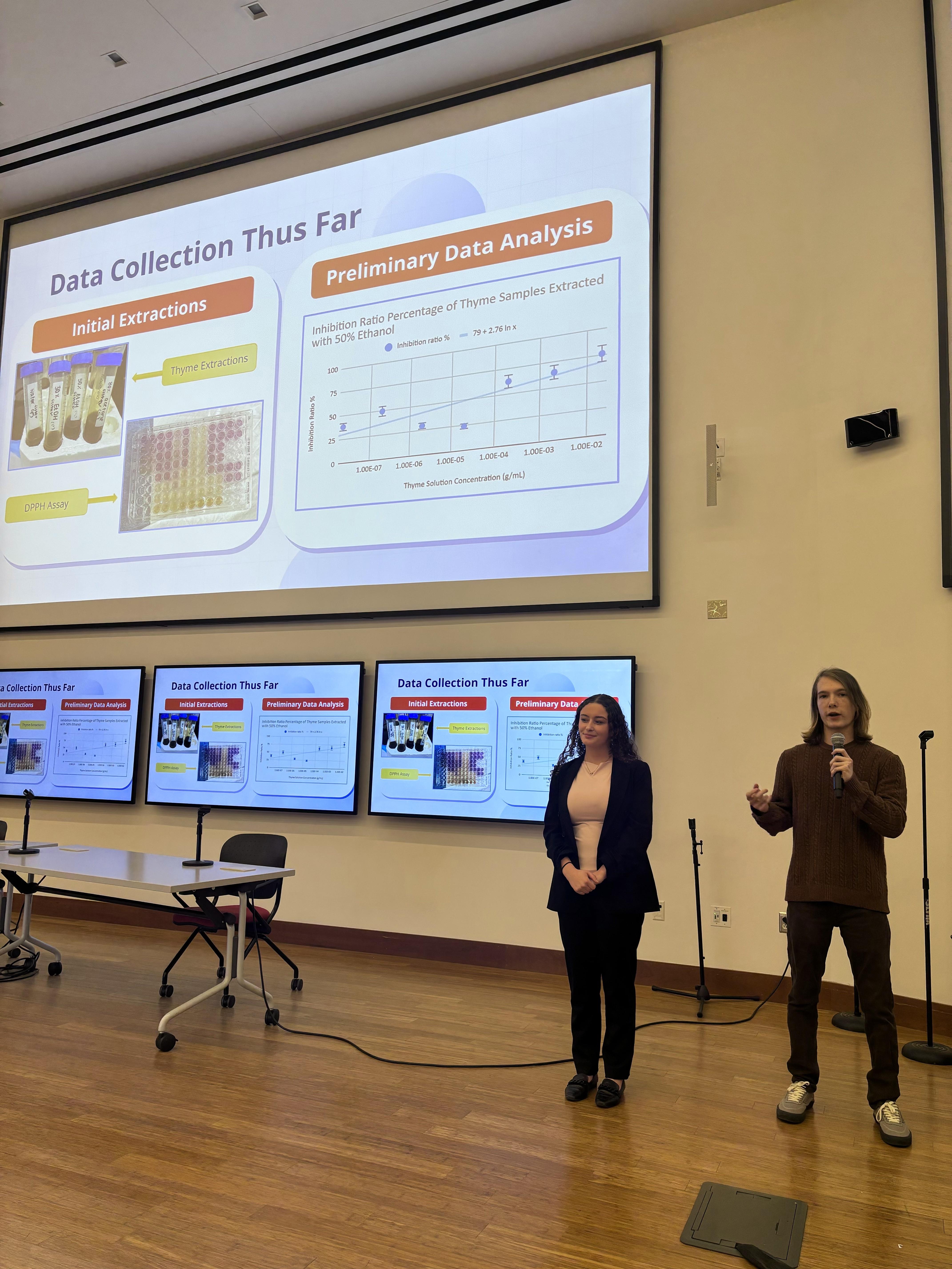 Two students of Team TOXINS standing in front of a presentation in a lecture hall.