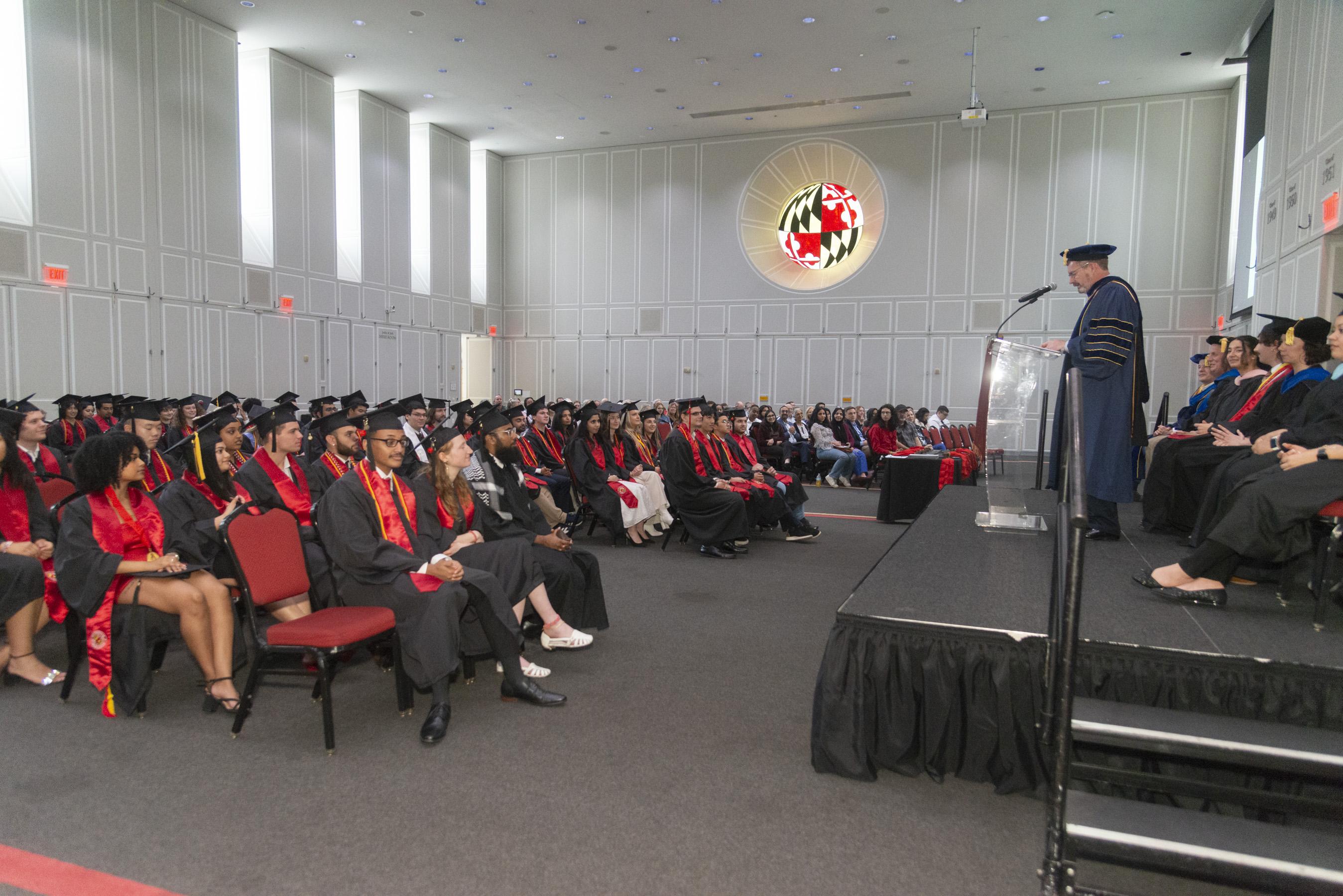 Side view of rows of students seated at graduation and podium in front