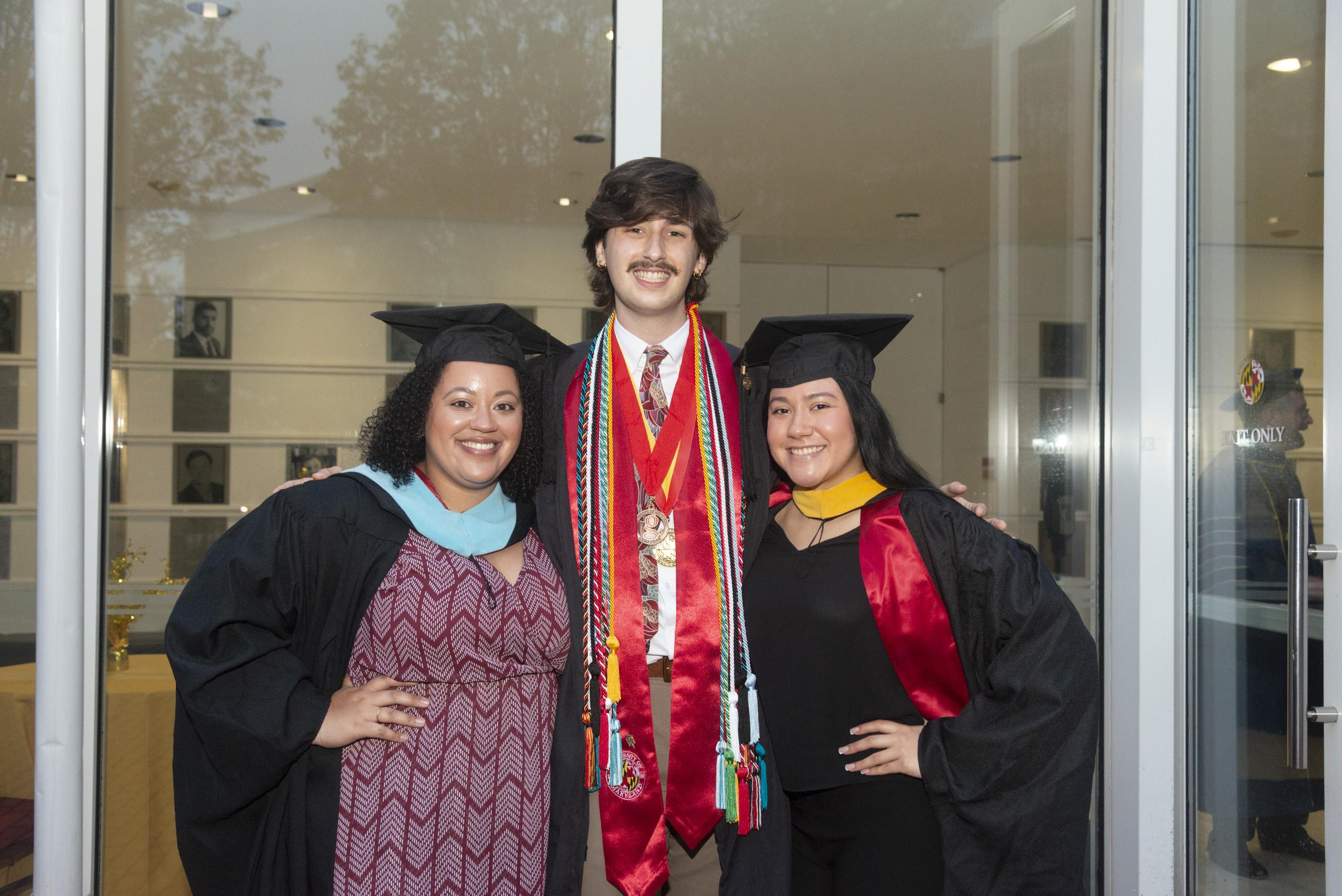 Two Gemstone staff members in regalia posing for photo with graduating student