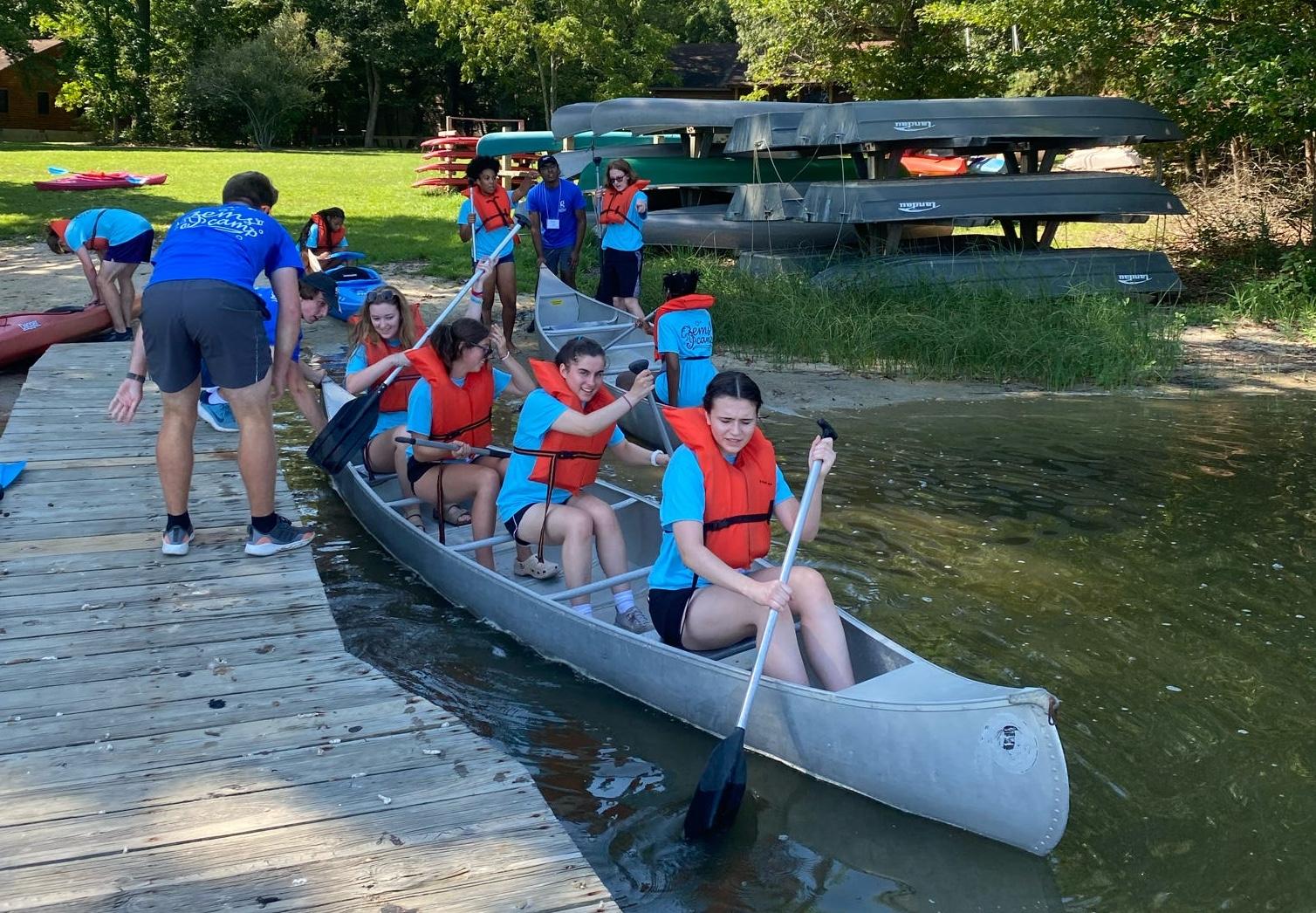 Four students wearing blue shirts and red life jackets in a canoe holding oars