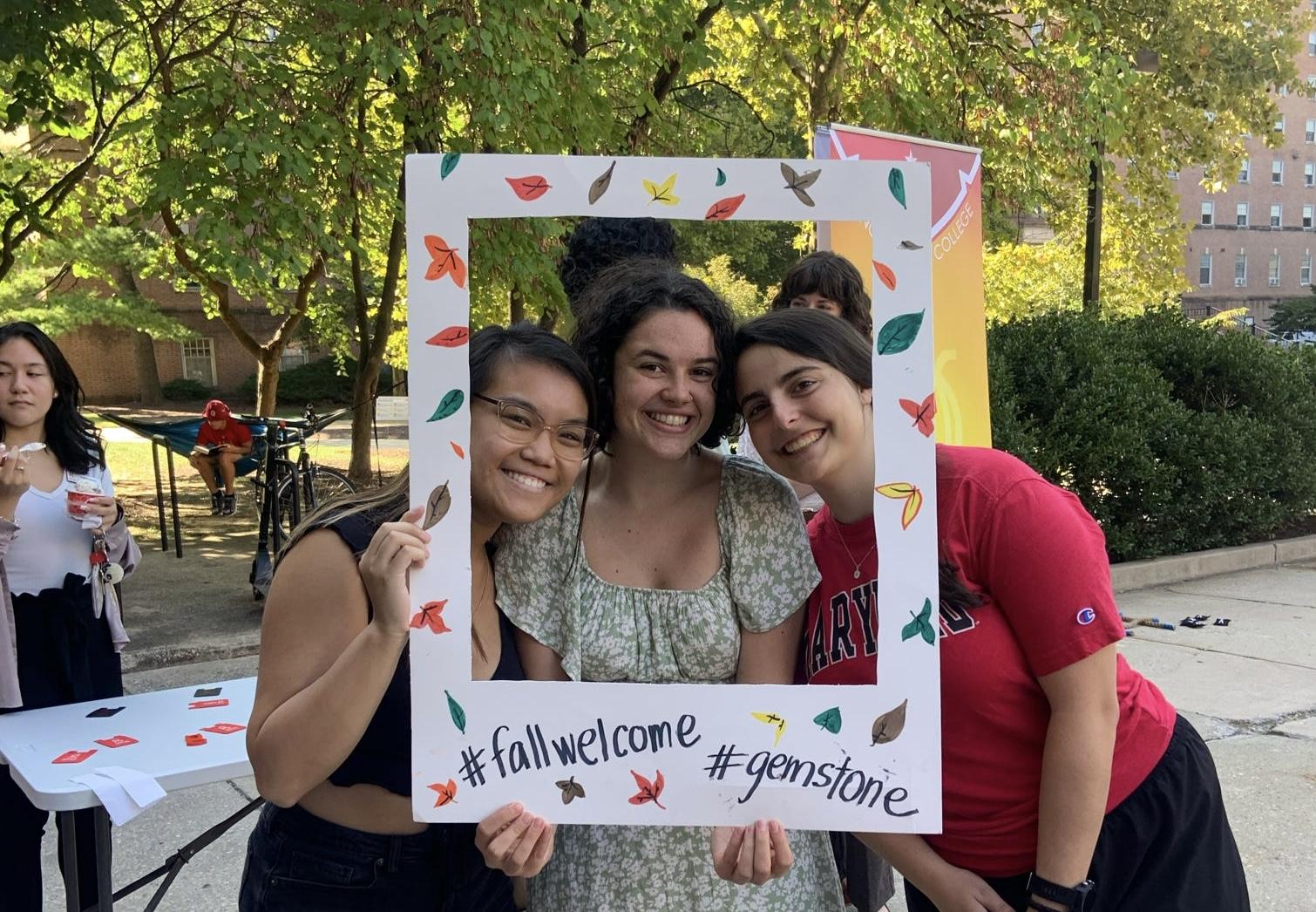 Three students holding photo frame cutout that says #fallwelcome #gemstone