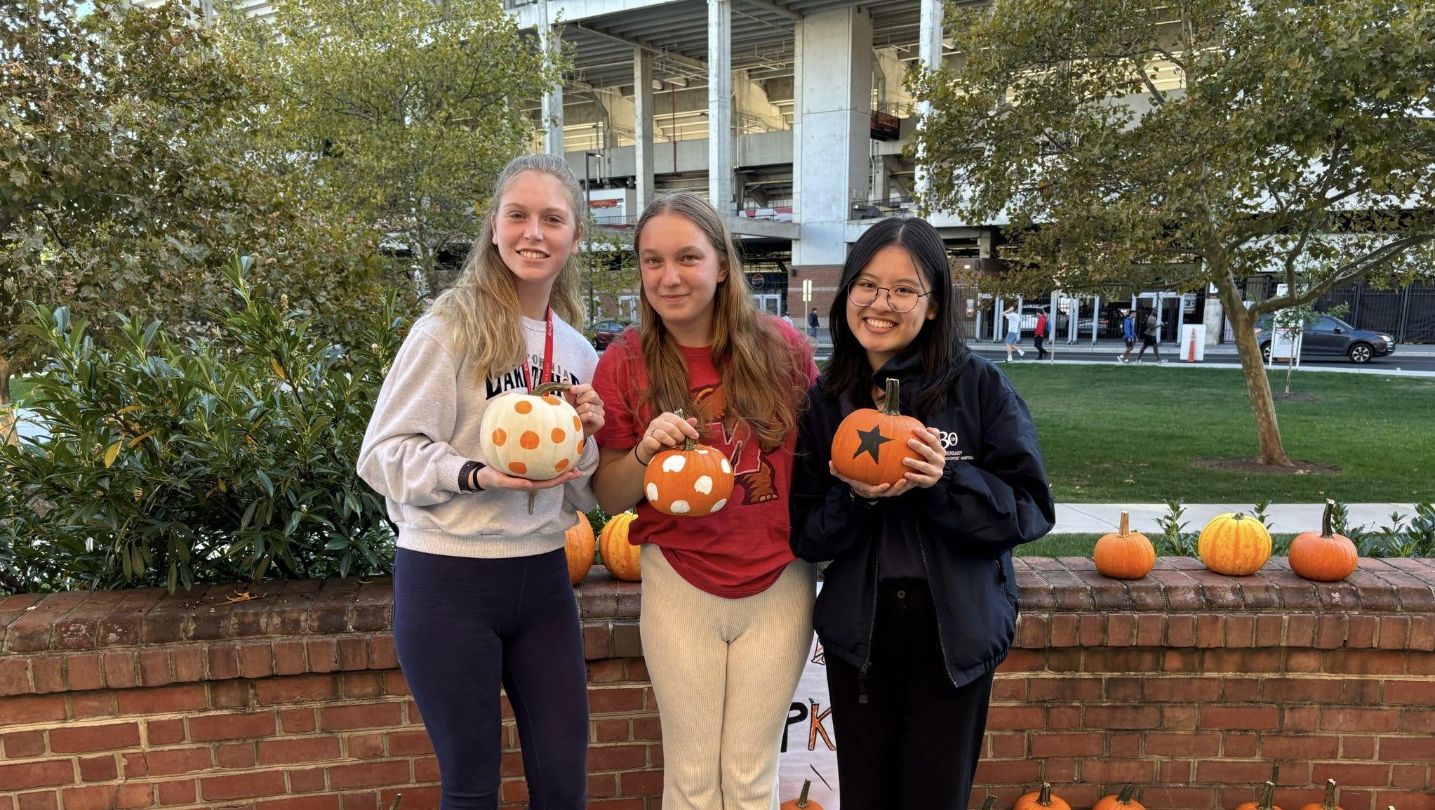 Three students smiling and holding painted pumpkins