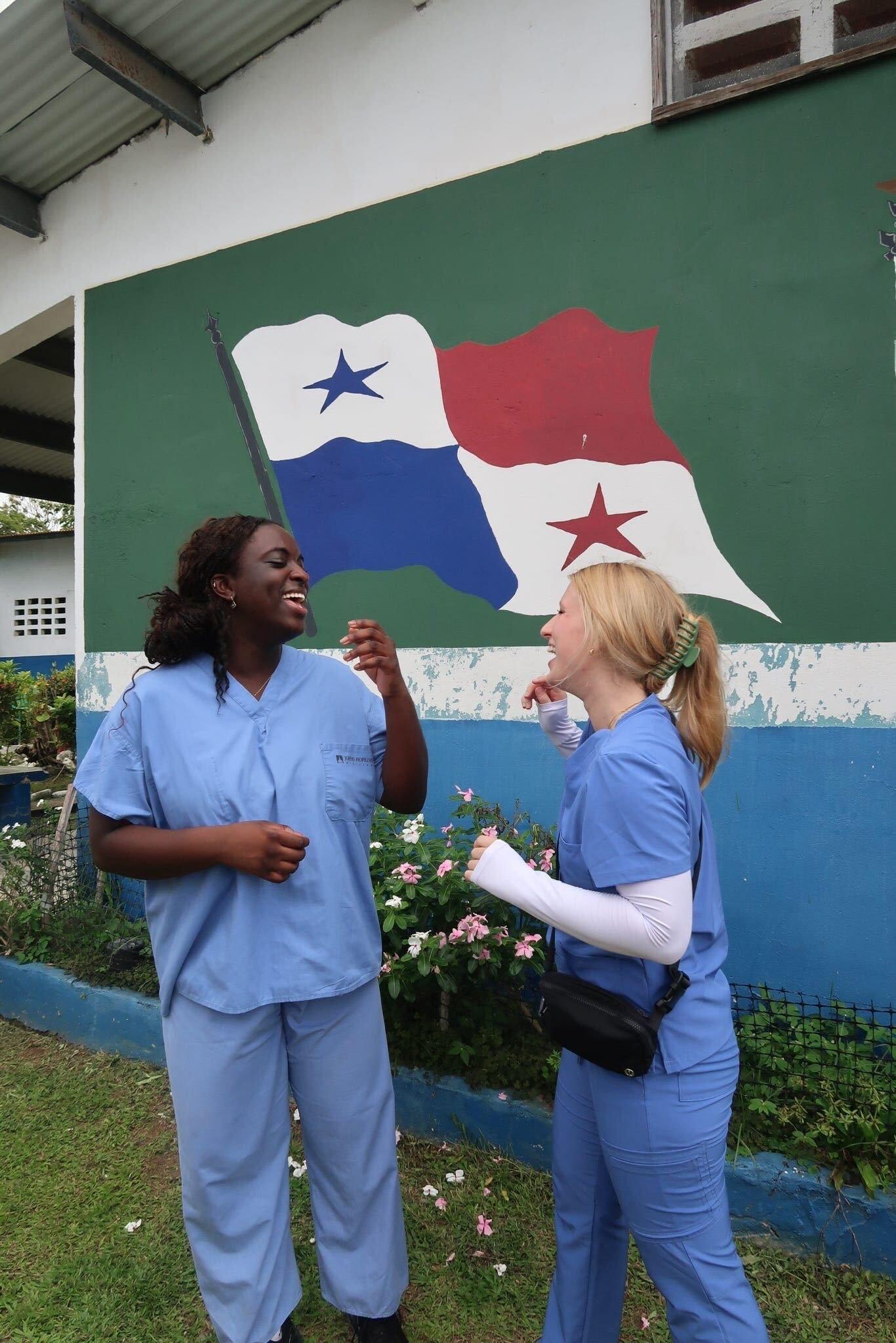 Tami Mumuney and another student wearing blue scrubs standing in front of mural of Panama flag
