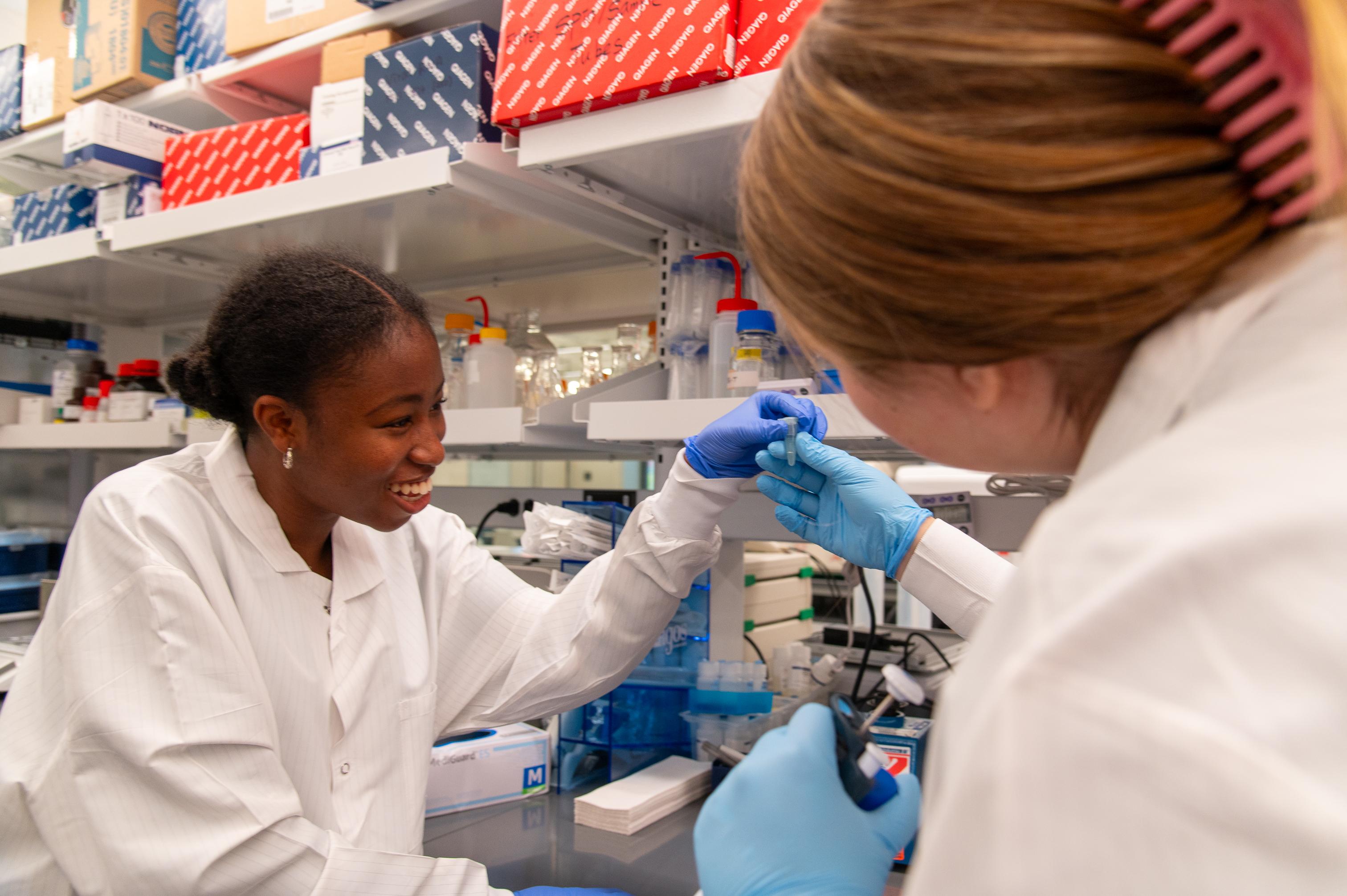 Two student researchers in white lab coats holding a microfuge tube
