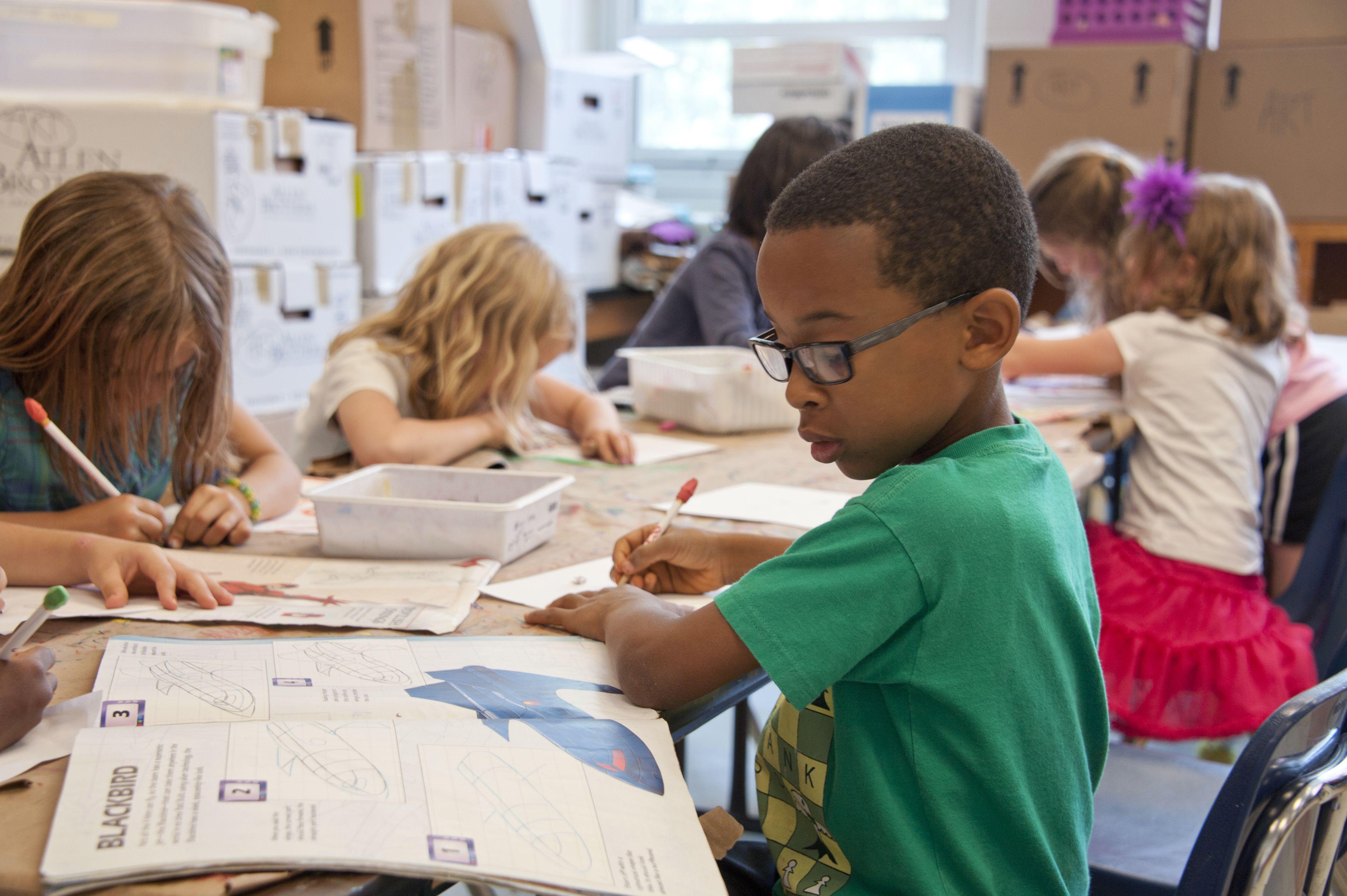 Children seated a table in a classroom reading and writing in workbooks
