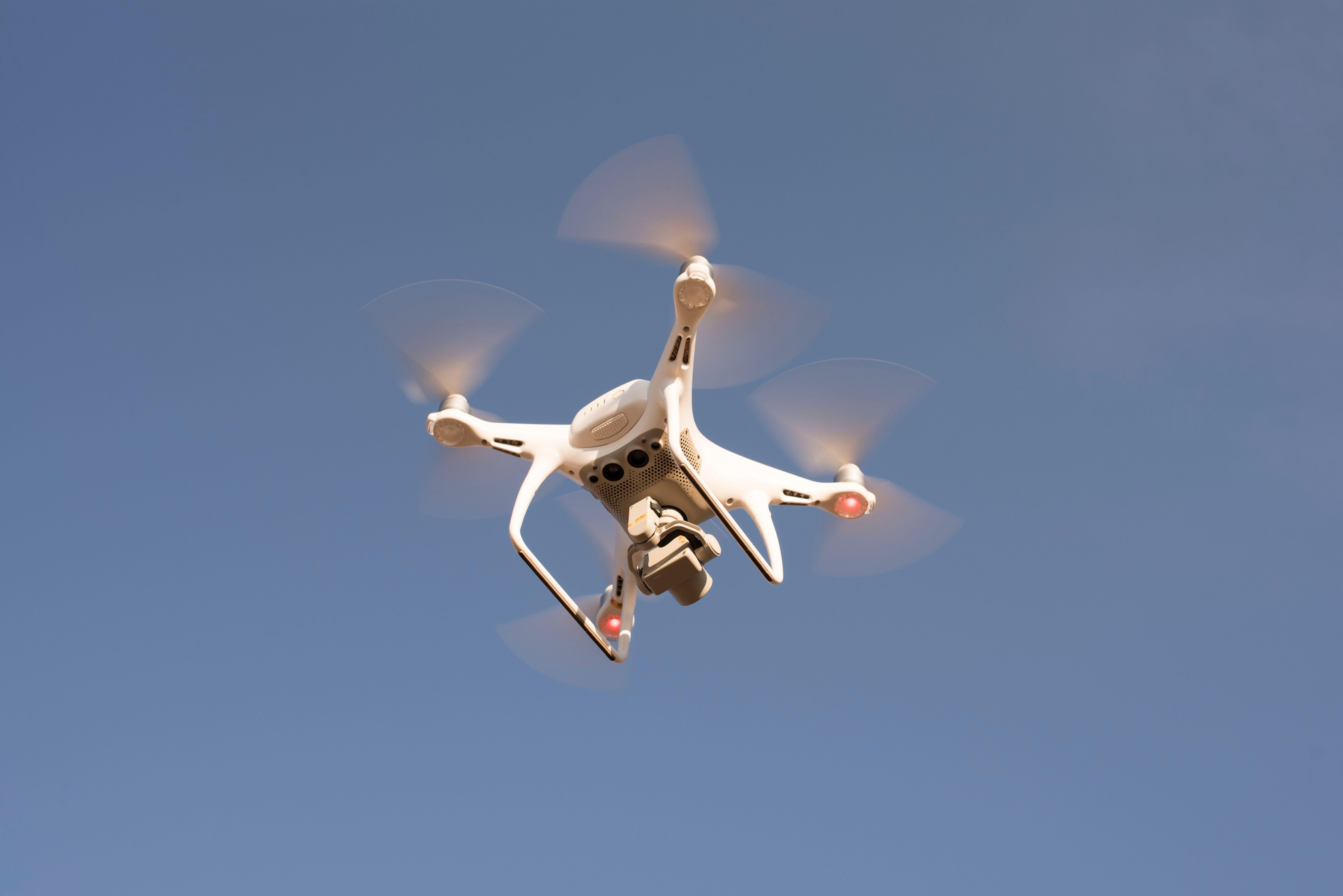 White drone flying in the air against blue sky backdrop